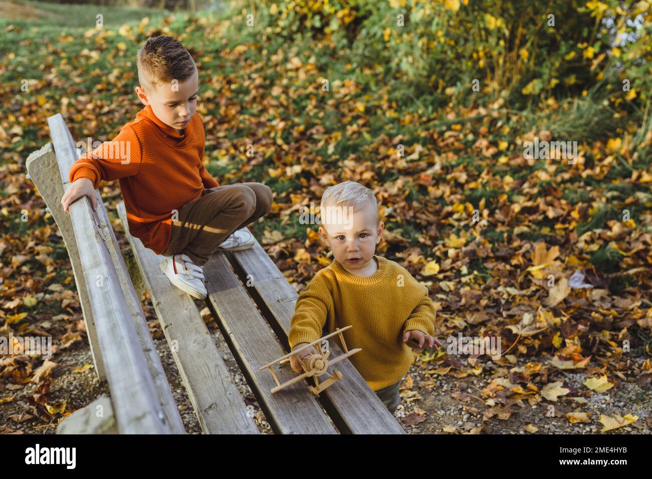 Der Junge sieht den Bruder an, der im Herbst mit einem Spielzeugflugzeug auf einer Bank spielt Stockfoto