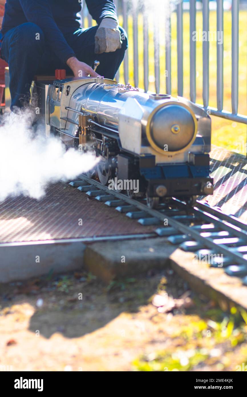 Winziges Spielzeug echte, alte Dampflokomotive, die auf einer Eisenbahnstrecke mit Fahrer auf dem Rücksitz fährt Stockfoto