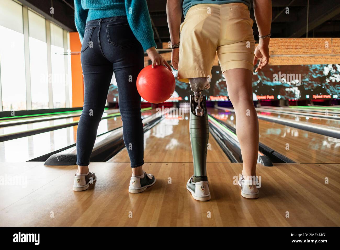 Eine Frau, die mit einer Freundin Ball hält und künstliche Gliedmaßen trägt, steht auf dem Parkettboden in der Bowlingbahn Stockfoto