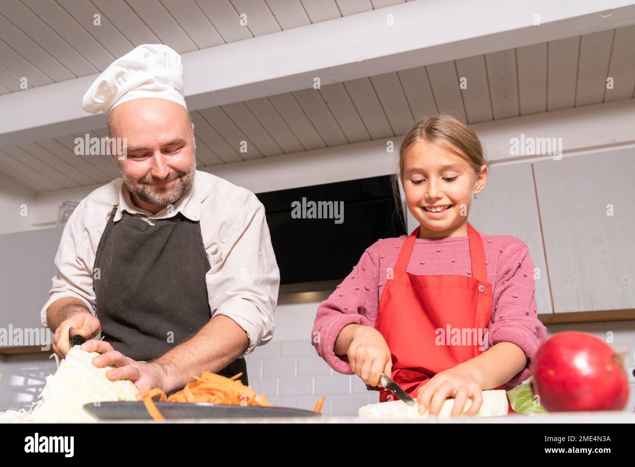 Vater und Tochter tragen Schürzen, die zu Hause in der Küche eine gesunde Mahlzeit zubereiten Stockfoto