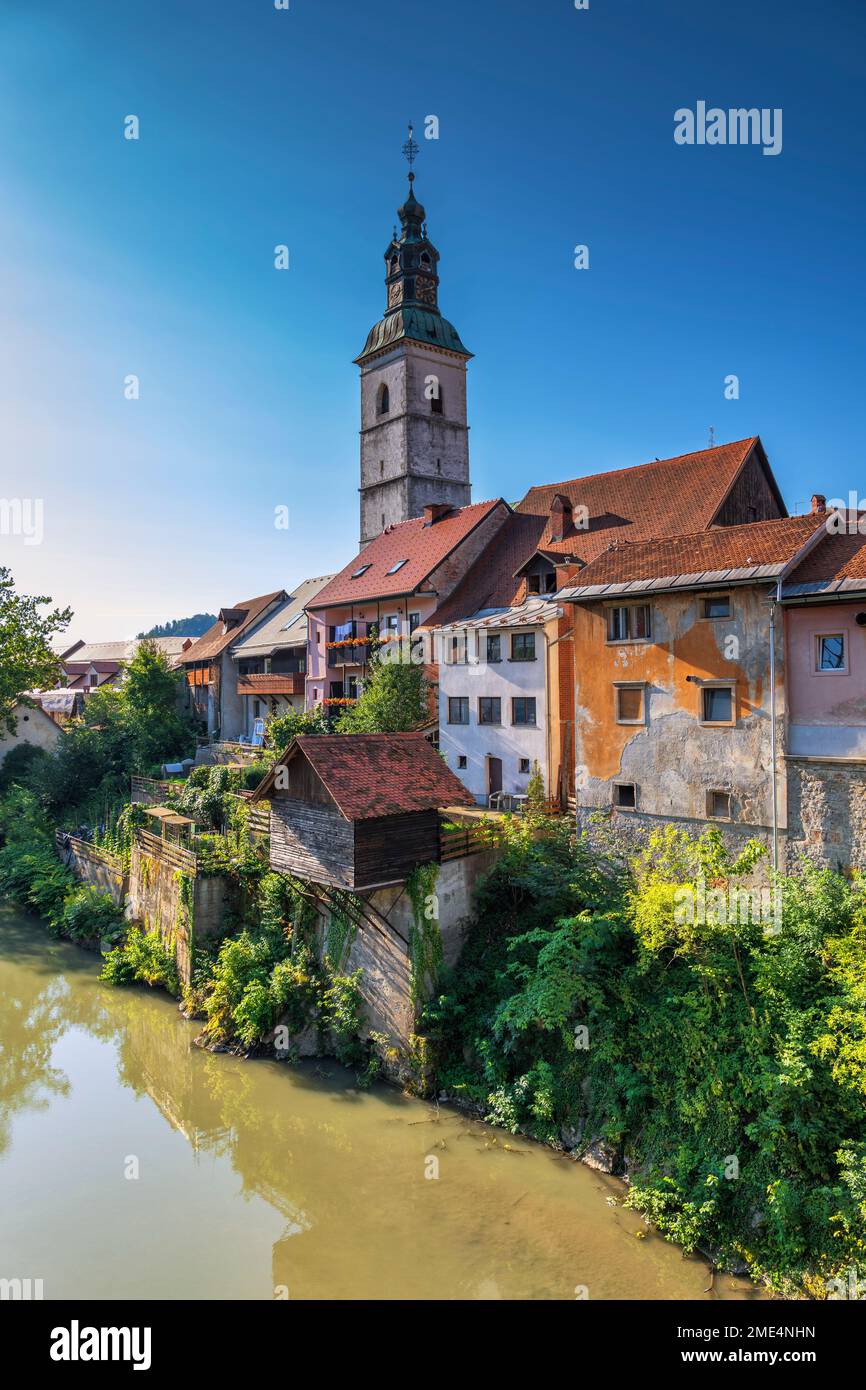 Slowenien, Oberkarniola, Skofja Loka, Häuser am Flussufer mit Glockenturm von St. Jacob Church im Hintergrund Stockfoto