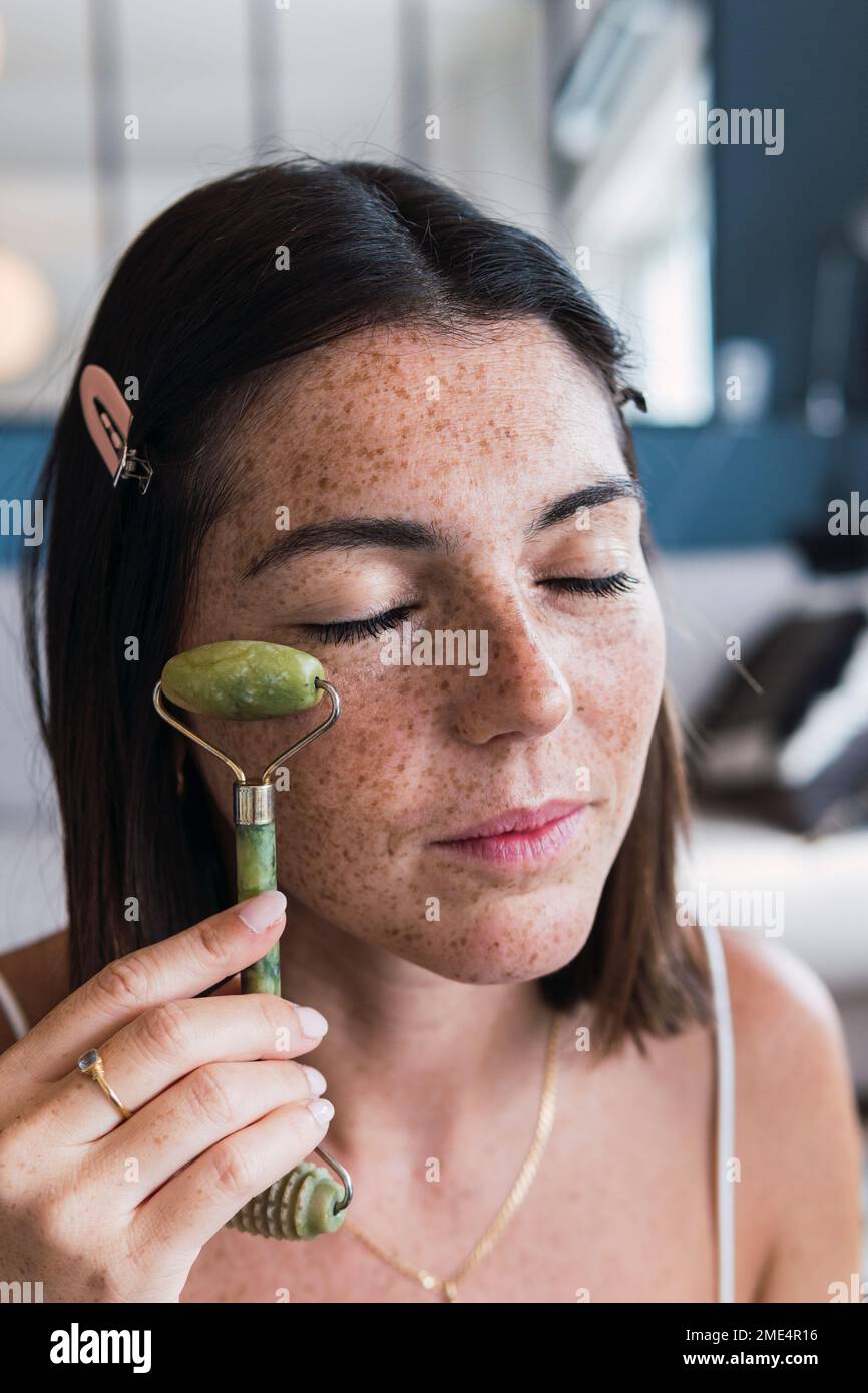 Junge Frau mit geschlossenem Augen massiert Gesicht mit Jade-Steinwalze Stockfoto