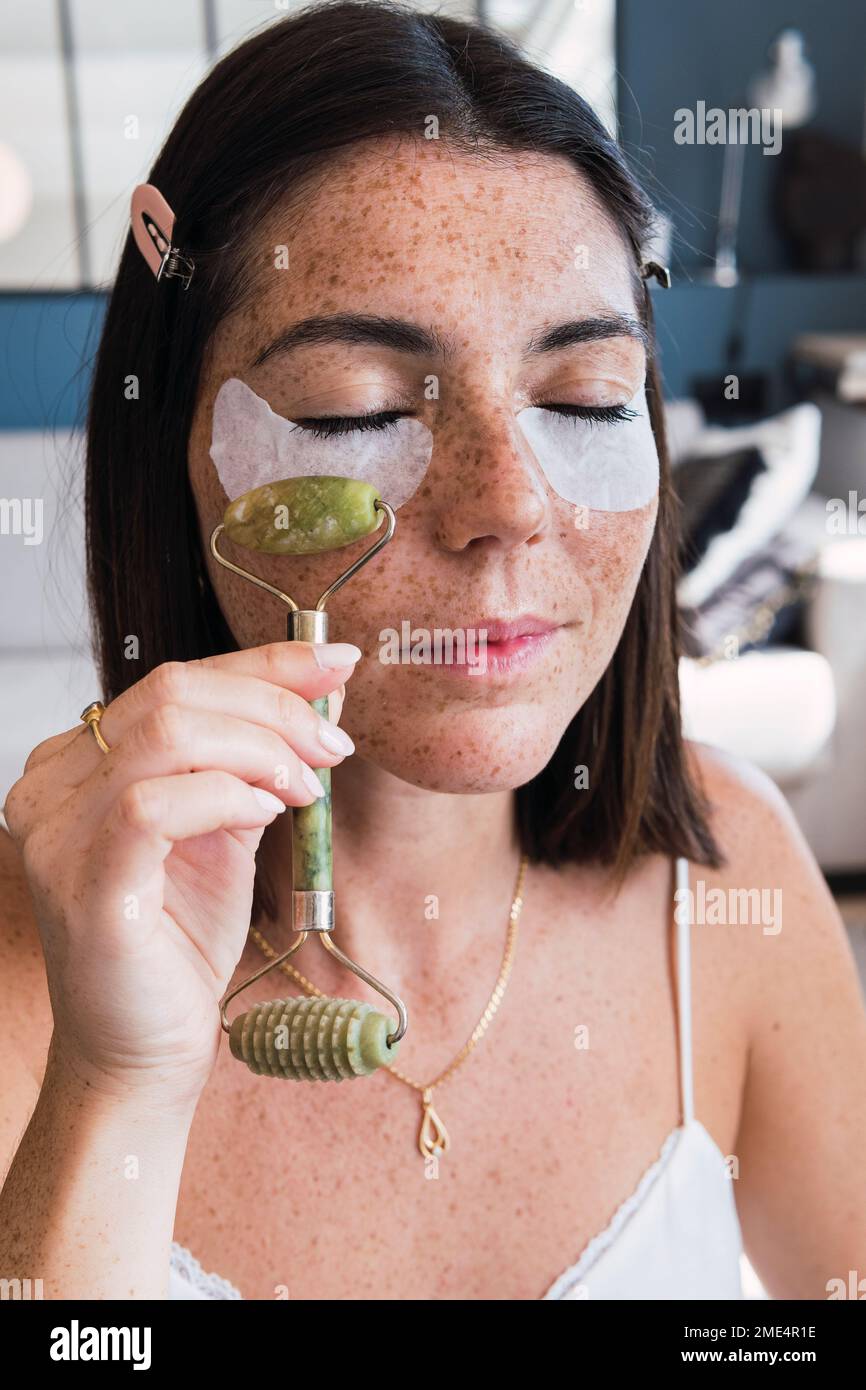 Frau mit Unteraugenflicken-Massage mit Jade-Steinwalze im Gesicht zu Hause Stockfoto