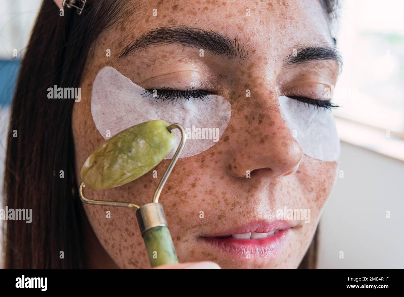 Frau mit Sommersprossen-Gesichtsmassage mit Jadesteinwalze Stockfoto