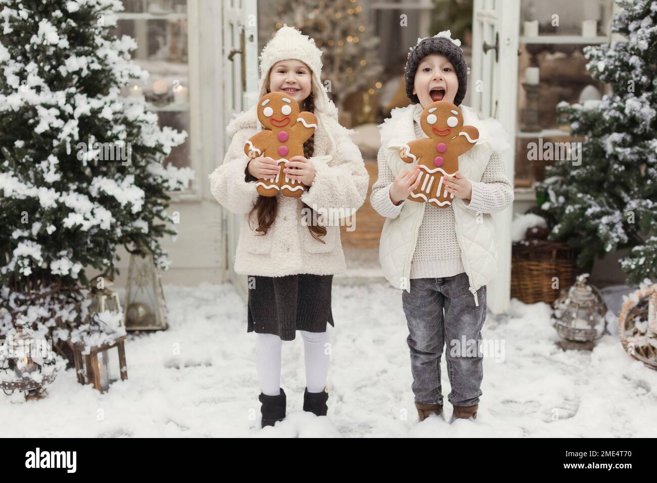 Glückliche Geschwister stehen mit Lebkuchenkeksen vor dem Haus Stockfoto