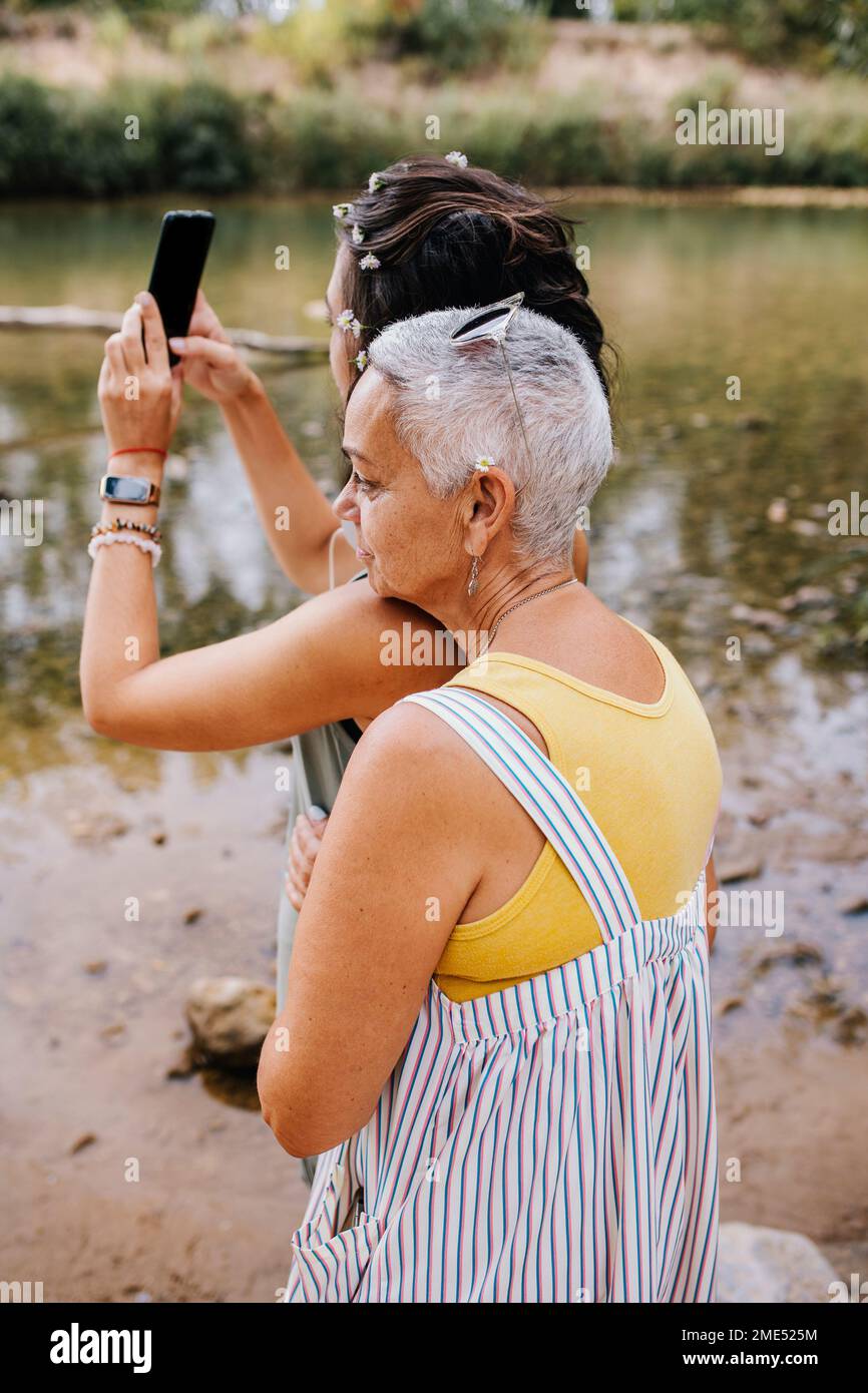 Frauen machen Selfie durch Mobilgeräte am Seeufer Stockfoto