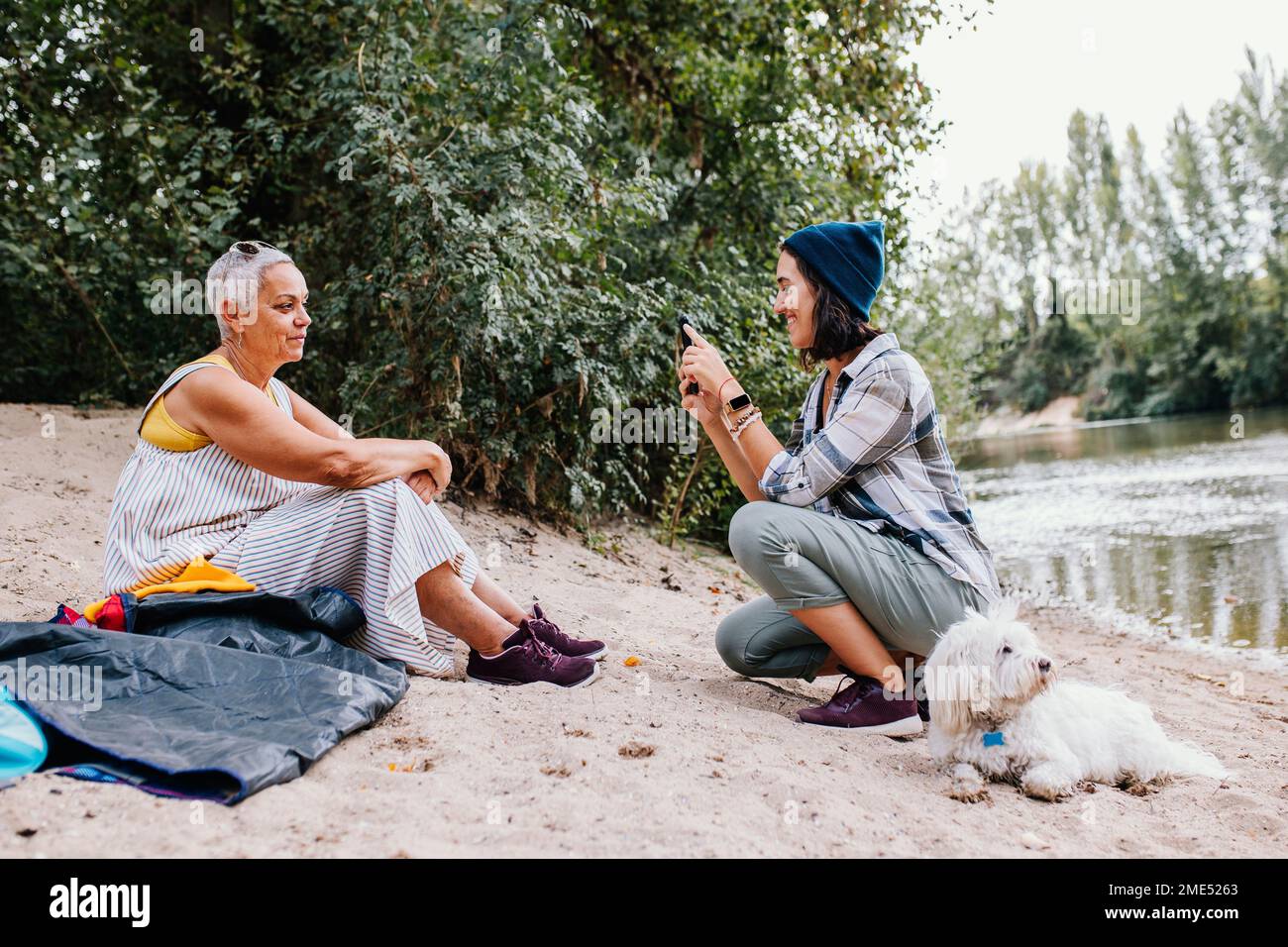 Junge Frau klickt Fotos von einem Freund mit Hund, der im Park sitzt Stockfoto