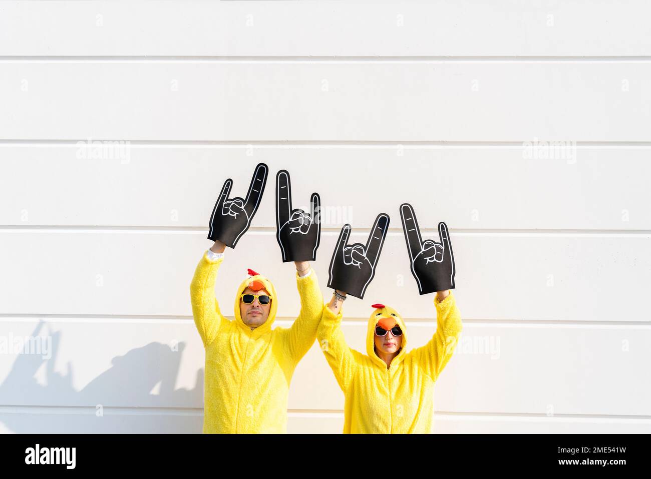 Verspielte Freunde in Hühnerkostümen stehen mit erhobenen Armen vor der Wand Stockfoto