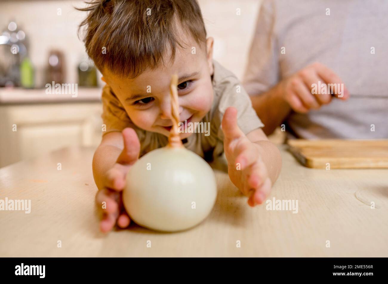 Glücklicher süßer Junge, der zu Hause weiße Zwiebeln auf der Küchentheke erreicht Stockfoto
