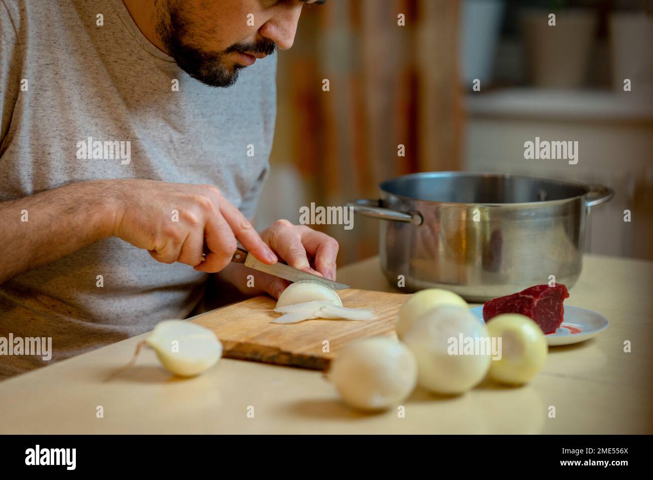 Mann hackt weiße Zwiebeln auf Schneidebrett in der Küche Stockfoto