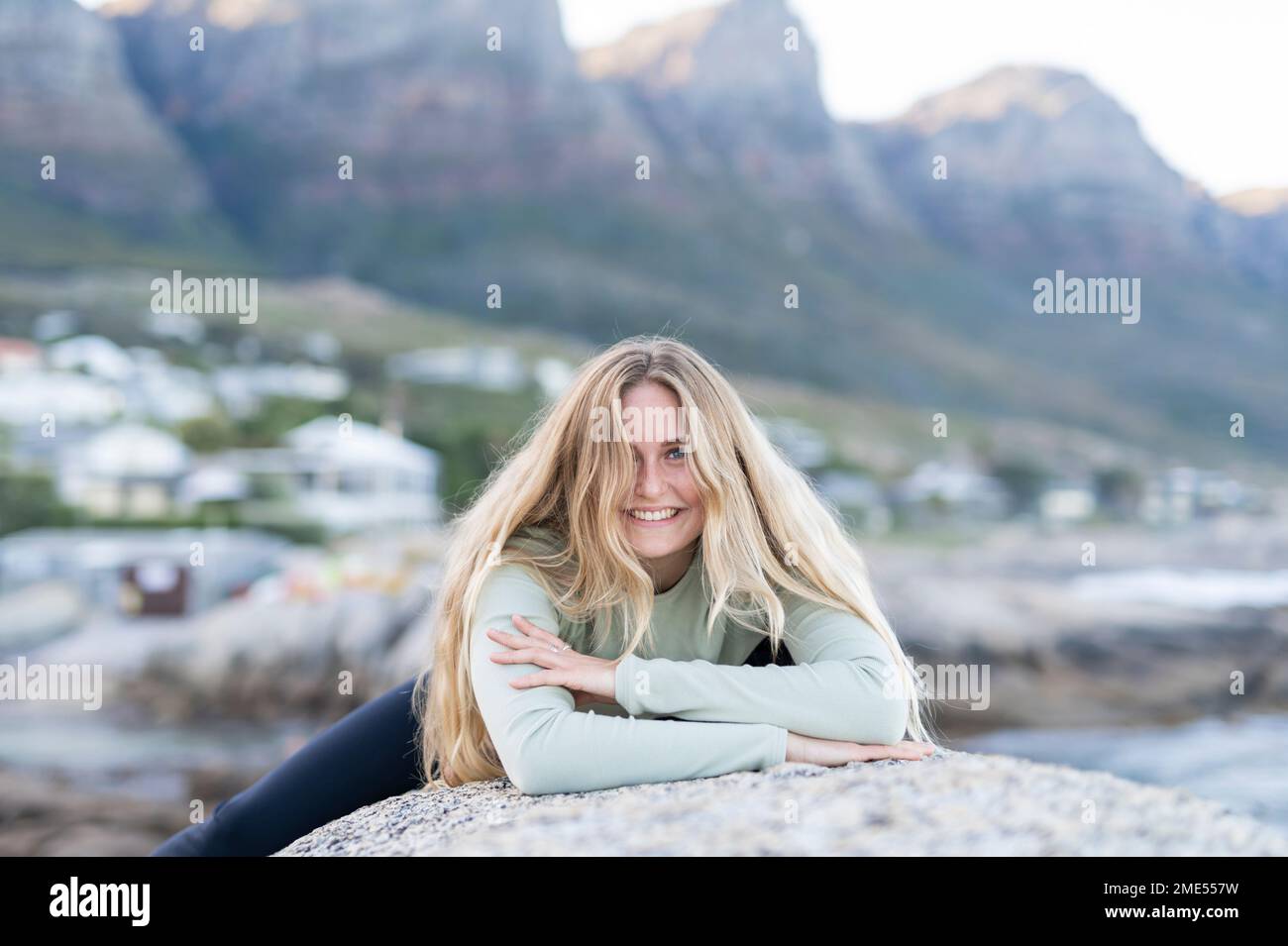 Lächelnde junge Frau mit blonden Haaren, die auf einem Stein lag Stockfoto