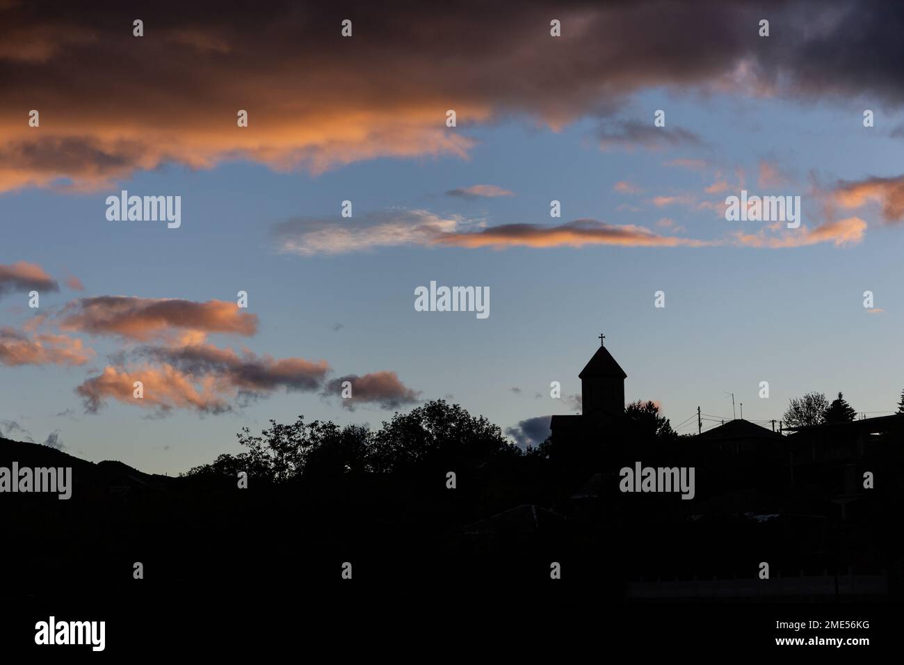 Die Silhouette des katholischen Kirchenglockens über den Baumwipfeln mit orangefarbenen Wolken im Sonnenuntergang am Himmel in Akhaltsikhe, Georgia. Stockfoto