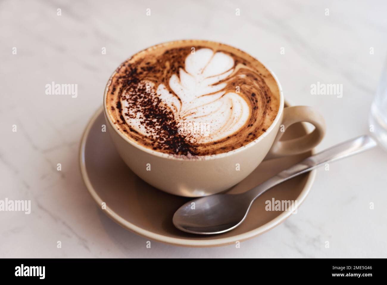 Nahaufnahme eines Cappuccinos in einem beigen Becher in einem Café - Kaffeekunst-Konzept Stockfoto