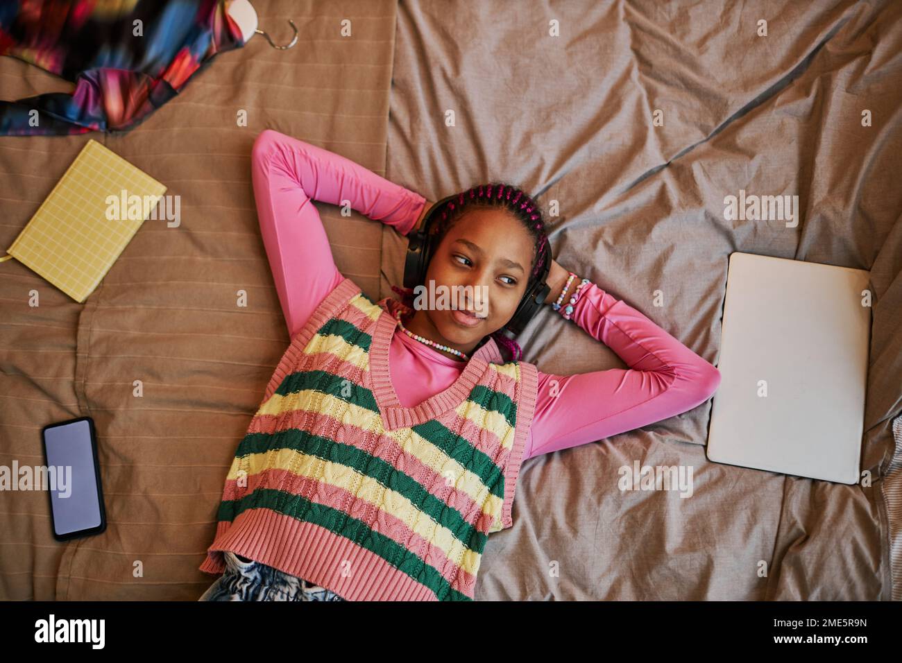 Blick von oben auf ein schwarzes Teenager-Mädchen, das auf dem Bett liegt und Musik mit Kopfhörern hört, Kopierraum Stockfoto