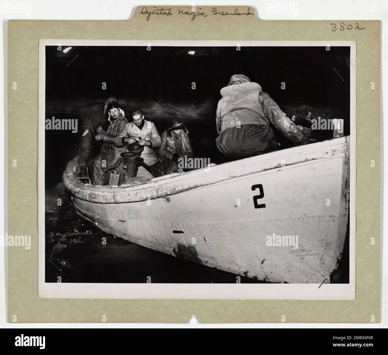 Niedergeworfene deutsche Gefangene sitzen still in einem kleinen Boot, während sie zu einem Kämpfer der Küstenwache vor der Küste Grönlands transportiert werden. Die Aktion fand statt, nachdem Mitarbeiter der Küstenwache die Nazis während der U-Boot-Kampagne im Atlantik gefangen nahmen. Stockfoto