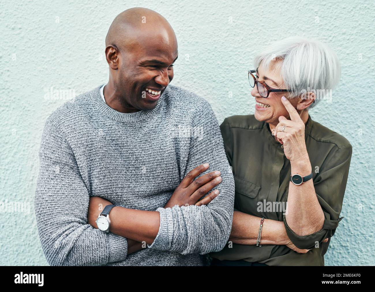 Wir haben nur unser eigenes kleines Verständnis. Zwei fröhliche, reife Geschäftsleute, die sich im Freien an einer Wand unterhalten. Stockfoto