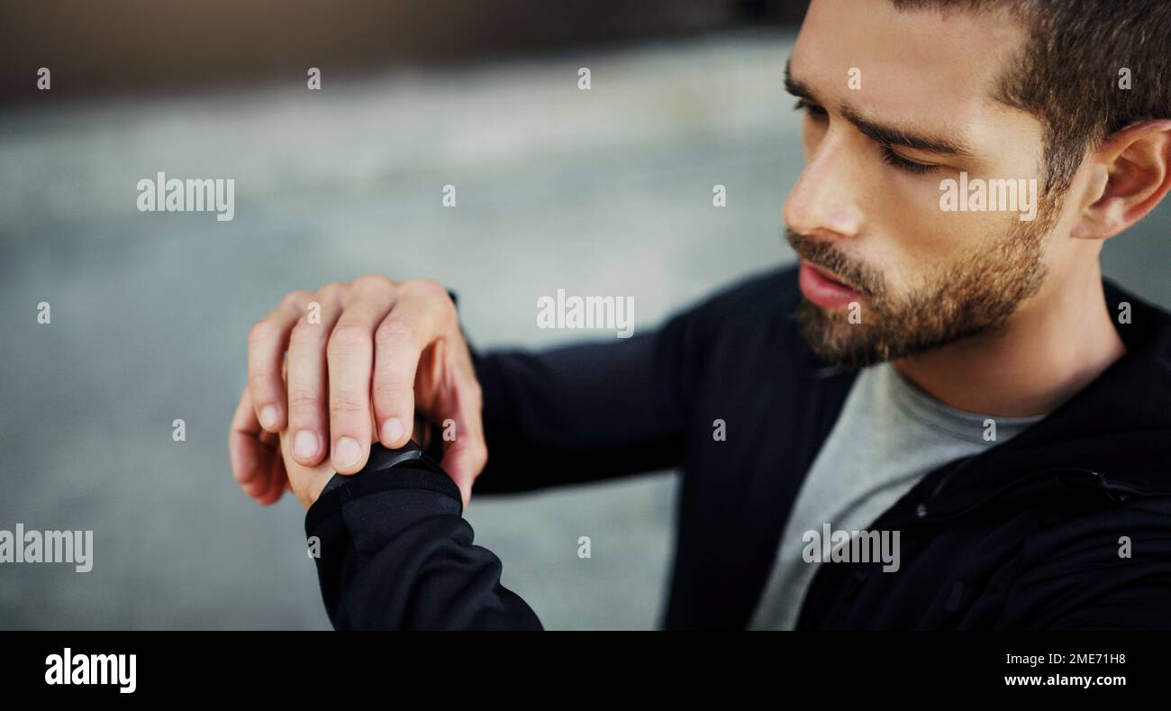 Halten Sie Ihre Fitness in Schach. Ein junger Mann, der auf seine Uhr schaut, während er in der Stadt trainiert. Stockfoto