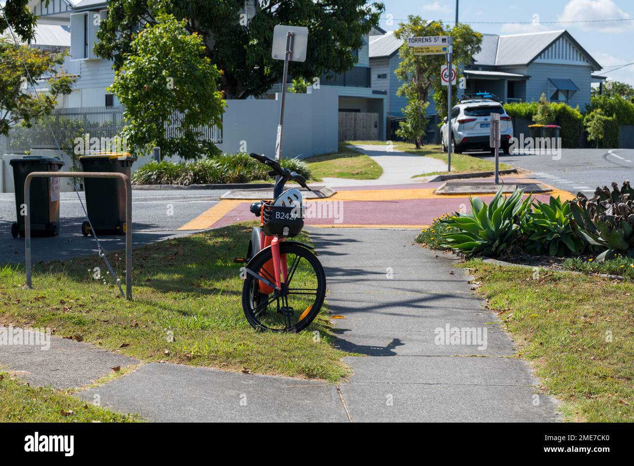 Brisbane, Australien – Januar 19 2023: Orangefarbenes E-Bike links am Fußweg in einem Wohngebiet, Blick von der Vorderseite des E-Bike Stockfoto