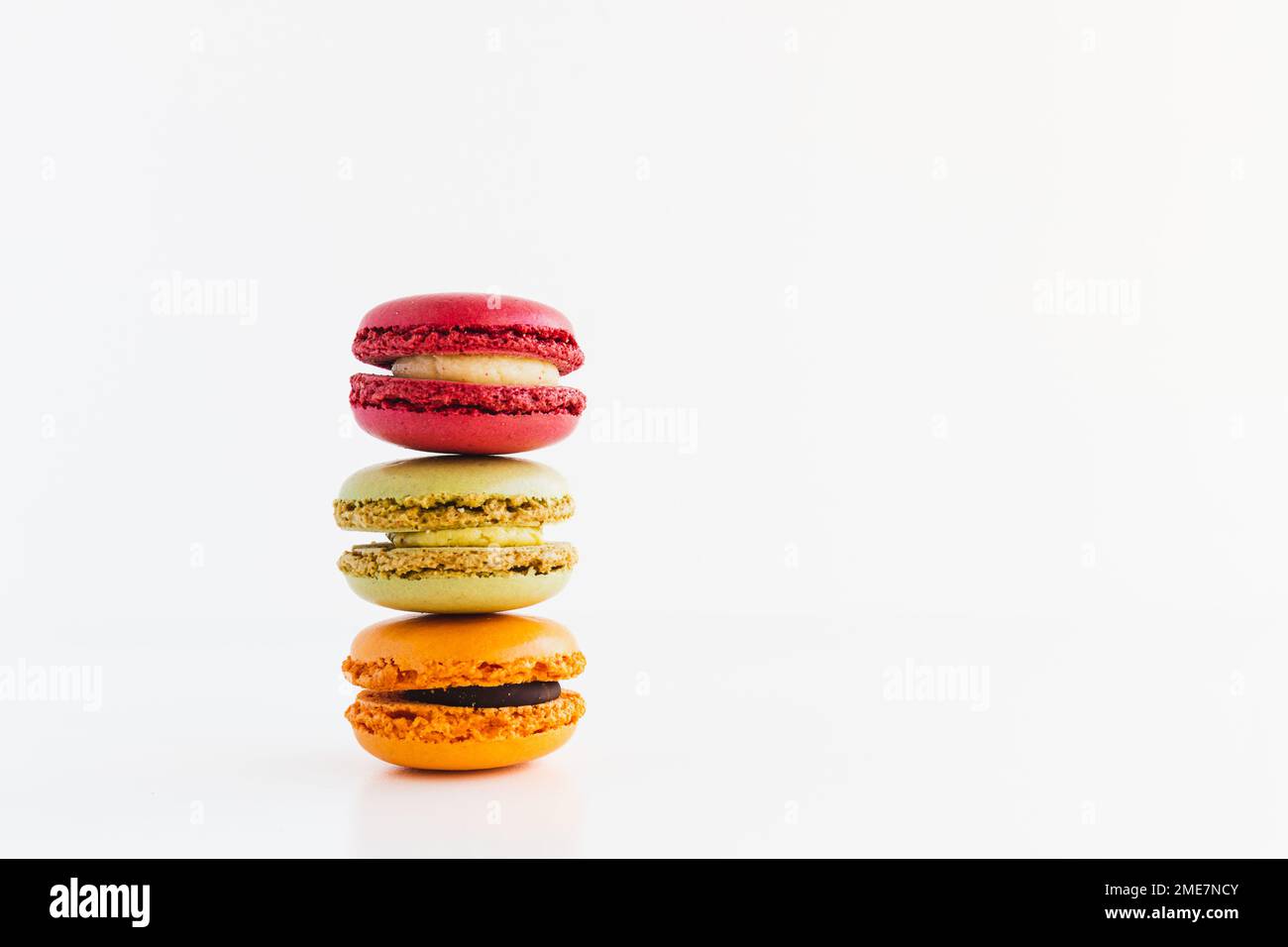 Ein Stapel roter Samt-, Pistachio-, Schokoladen- und Mandarin-Macaron-Kekse auf weißem Hintergrund Stockfoto