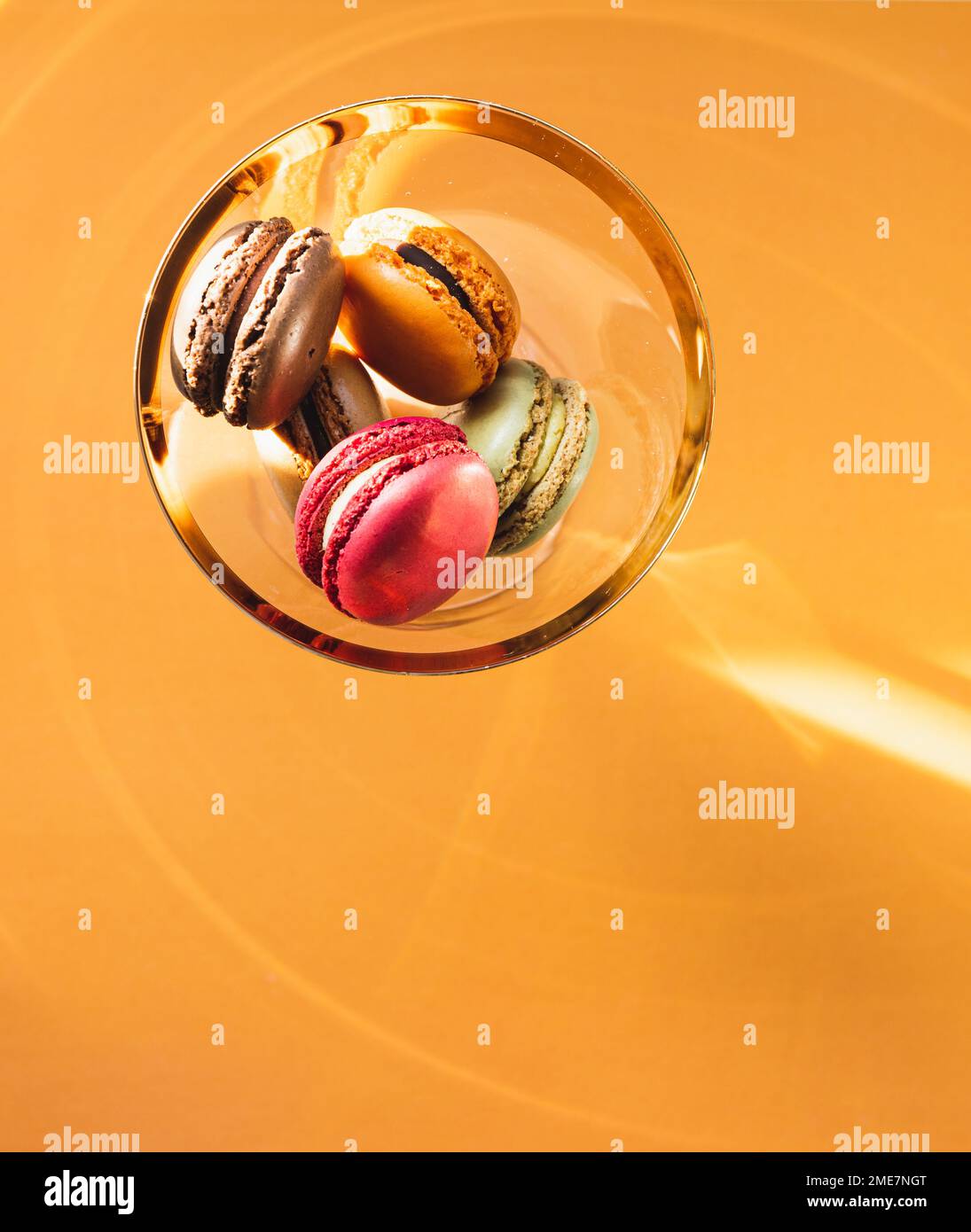 Farbenfrohe Macaron-Kekse in goldenem Glas auf goldenem Hintergrund Stockfoto
