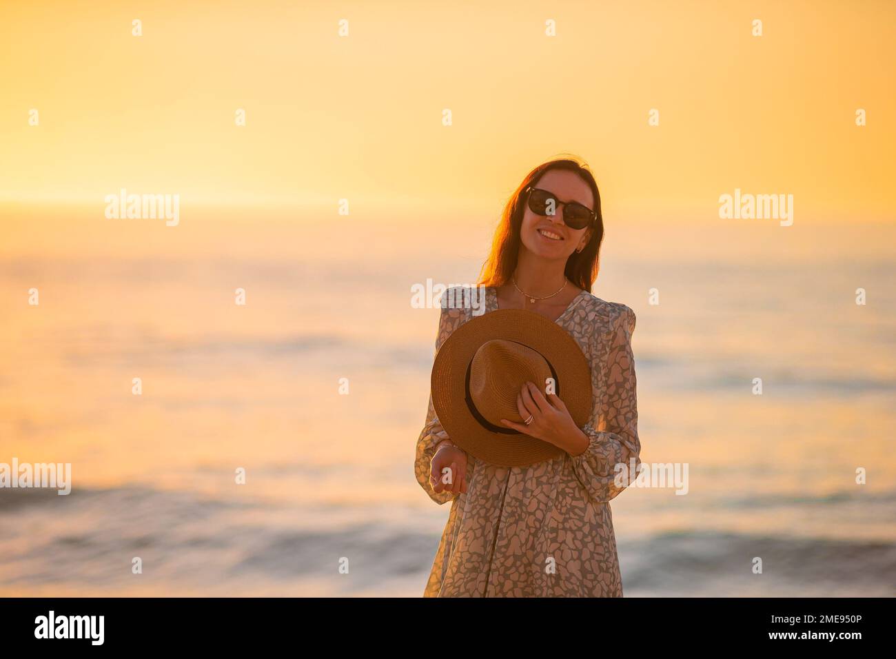 Junge wunderschöne Frau mit Strohhut am Strand bei Sonnenuntergang Stockfoto