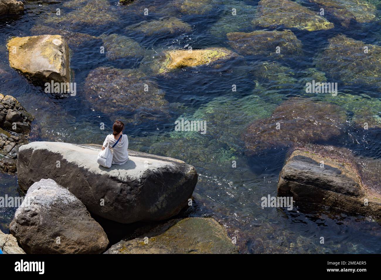 Solofrau sitzt auf Felsen im Ligurischen Meer, in Riomaggiore, Cinque Terre, Italien. Stockfoto