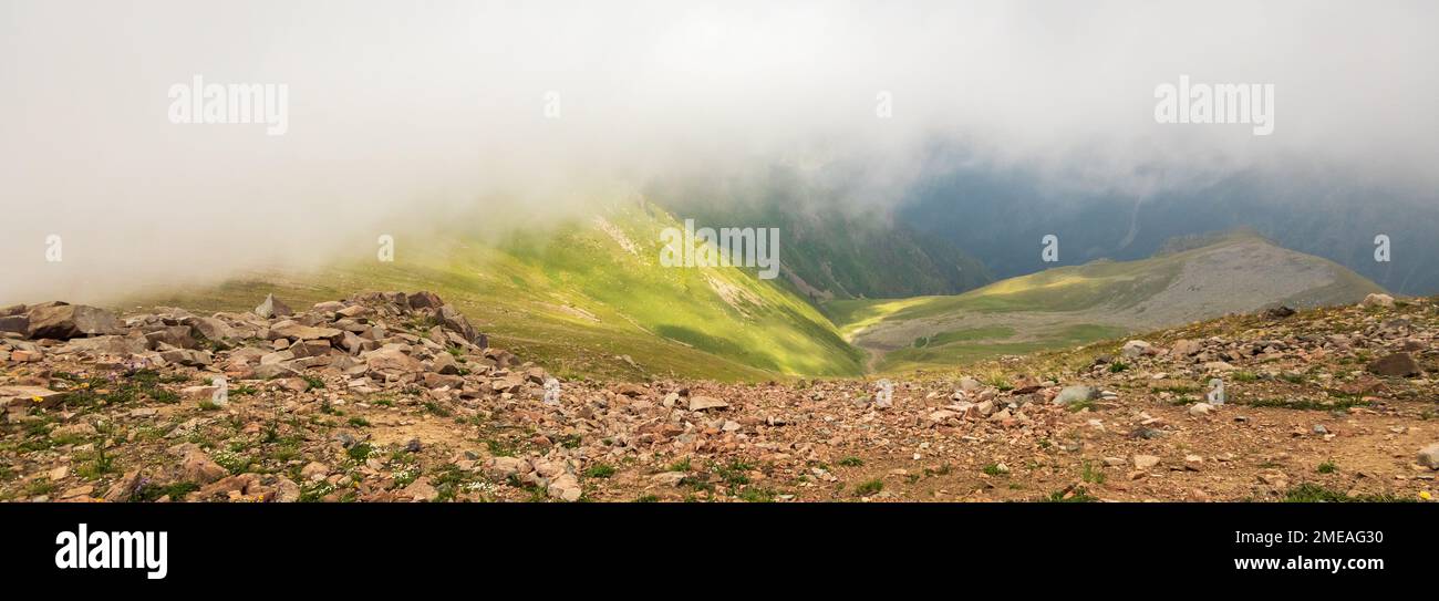 Geheimnisvolle minimalistische Berglandschaft in großer Höhe mit Wolken, die große Gipfel berühren. Bannerformat Stockfoto