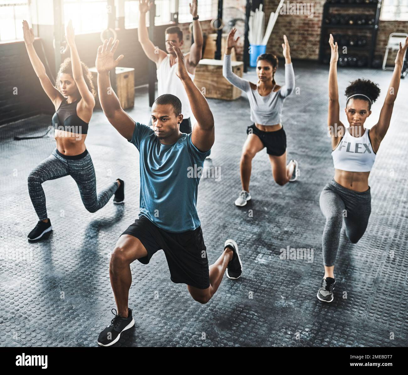 Ihr Workout auf die nächste Stufe bringen. Eine Gruppe junger Leute, die während ihres Trainings in einem Fitnessstudio Ausfallschritte machen. Stockfoto