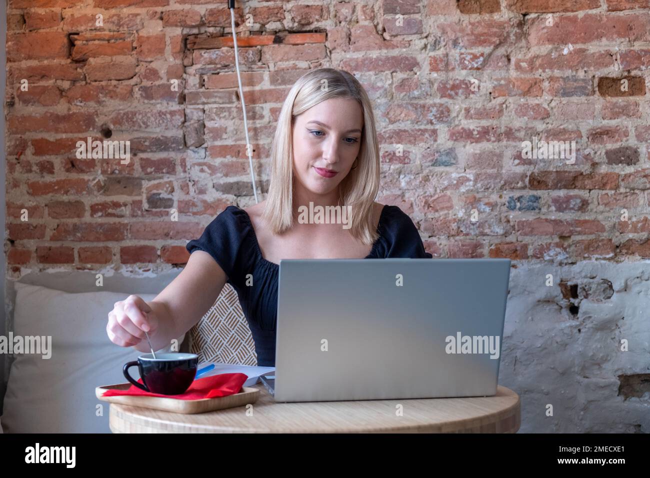 Wunderschöne weiße Frau, die von etwas träumt, während sie mit einem tragbaren Netzbuch in einer modernen Café-Bar sitzt, junge, charmante Freiberuflerin, die während der Arbeit an einem Laptop über neue Ideen nachdenkt. Hochwertiges Foto Stockfoto