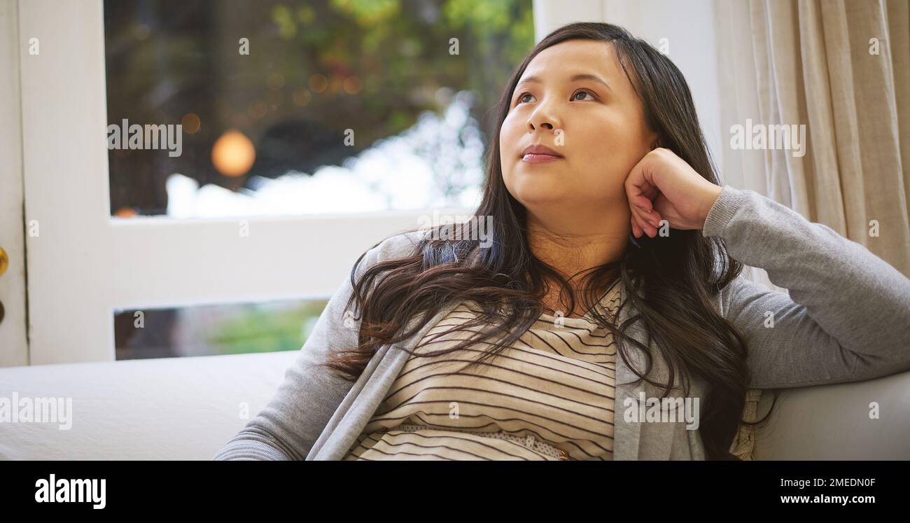 In all ihren Gedanken verloren. Eine attraktive junge Frau, die aufmerksam aussieht, während sie sich zu Hause entspannt. Stockfoto