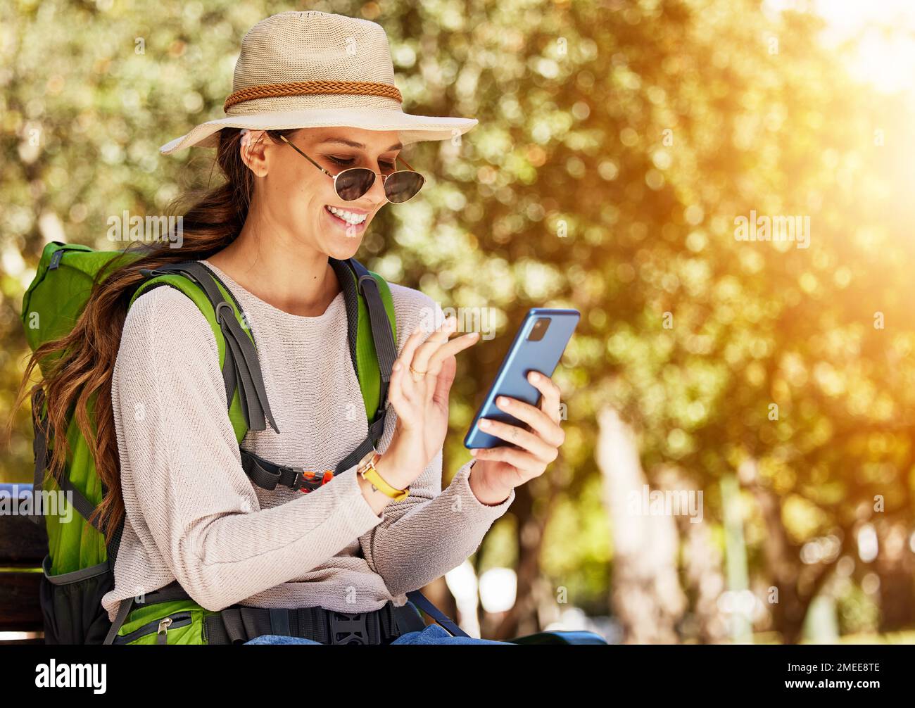 Glückliche Frau, Rucksack und Telefon auf Reisen, Sightseeing oder Abenteuer in Naturpark, Bäumen Wald oder Kanadas Wald. Lächeln, Tourismus und mobile Technologie Stockfoto