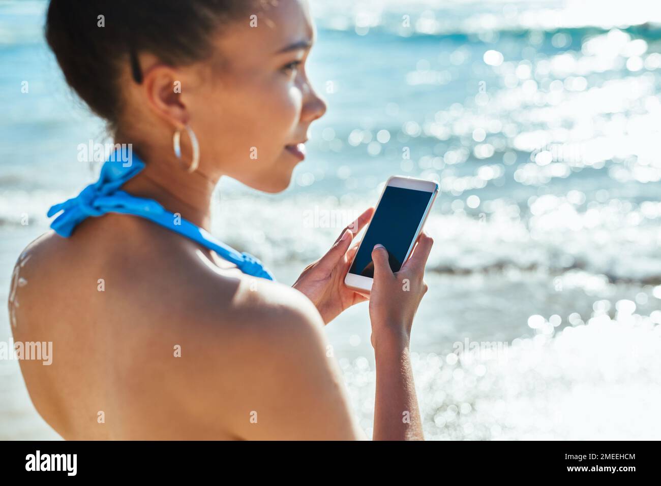 Der Strand, auch bekannt als Nature Hotspot. Eine wunderschöne junge Frau, die am Strand ein Handy benutzt. Stockfoto