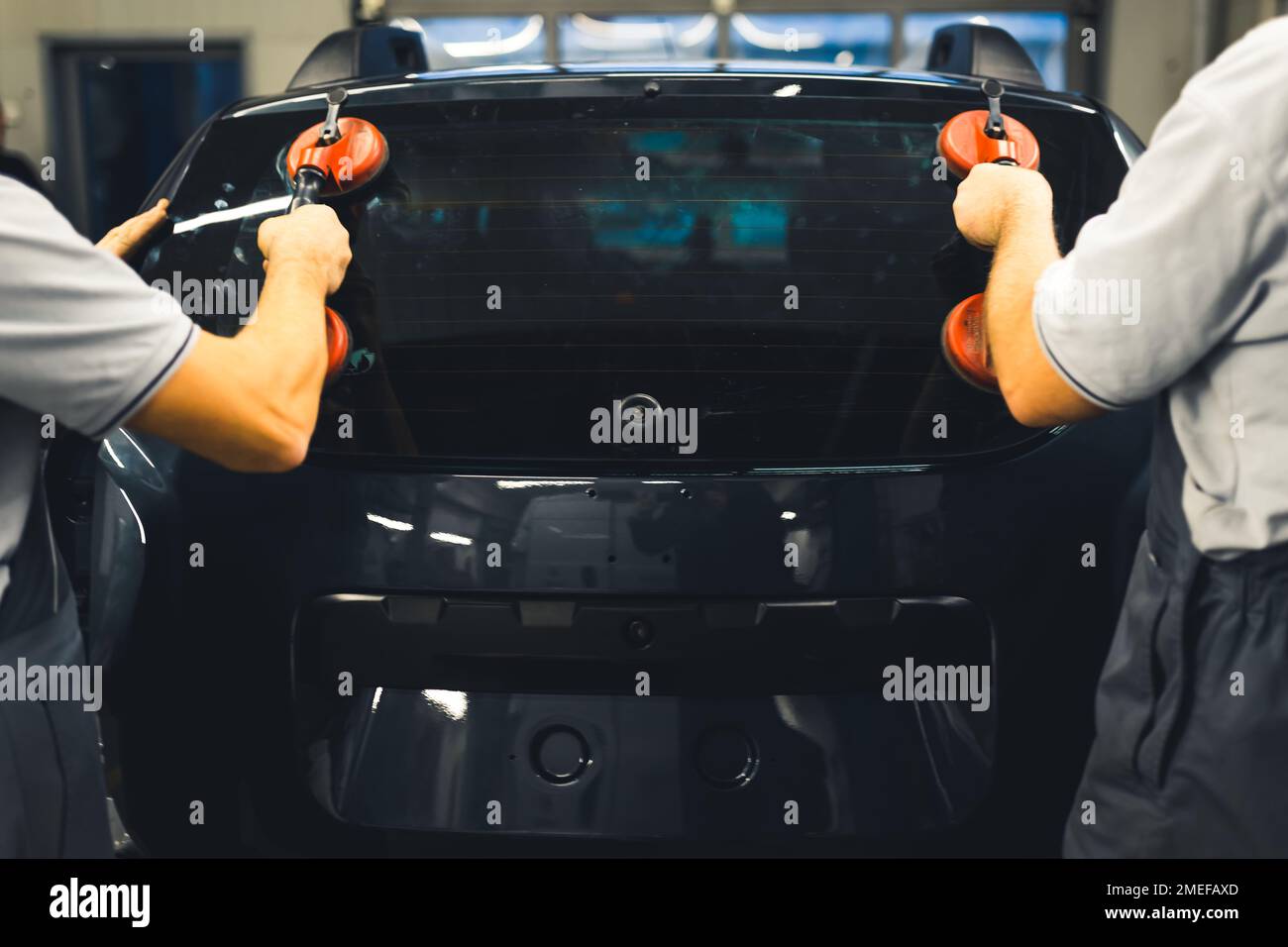 Rückansicht von zwei Männern, die die Heckscheibe mit professionellen Werkzeugen in das Fahrzeugheck einbauen. Garagenarbeiten. Fahrzeugwartung. Horizontale Indoor-Aufnahme. Hochwertiges Foto Stockfoto