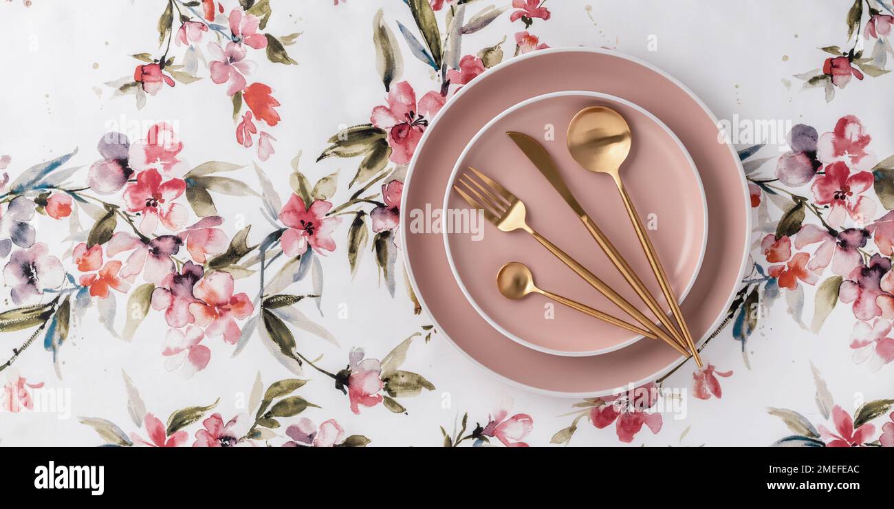 Beige runde Teller und goldenes Besteck auf einer weißen Tischdecke mit Blumenmuster, Blick von oben auf den Tisch. Flach liegendes Design. Keramikutensilien, Servieren. Ta Stockfoto