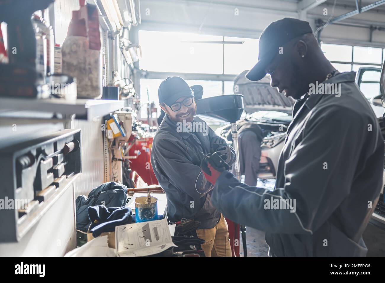Mittlere Aufnahme. Zwei männliche Mechaniker arbeiten zusammen, von einer Wokrbank und lächeln. Werkstattkonzept. Hochwertiges Foto Stockfoto