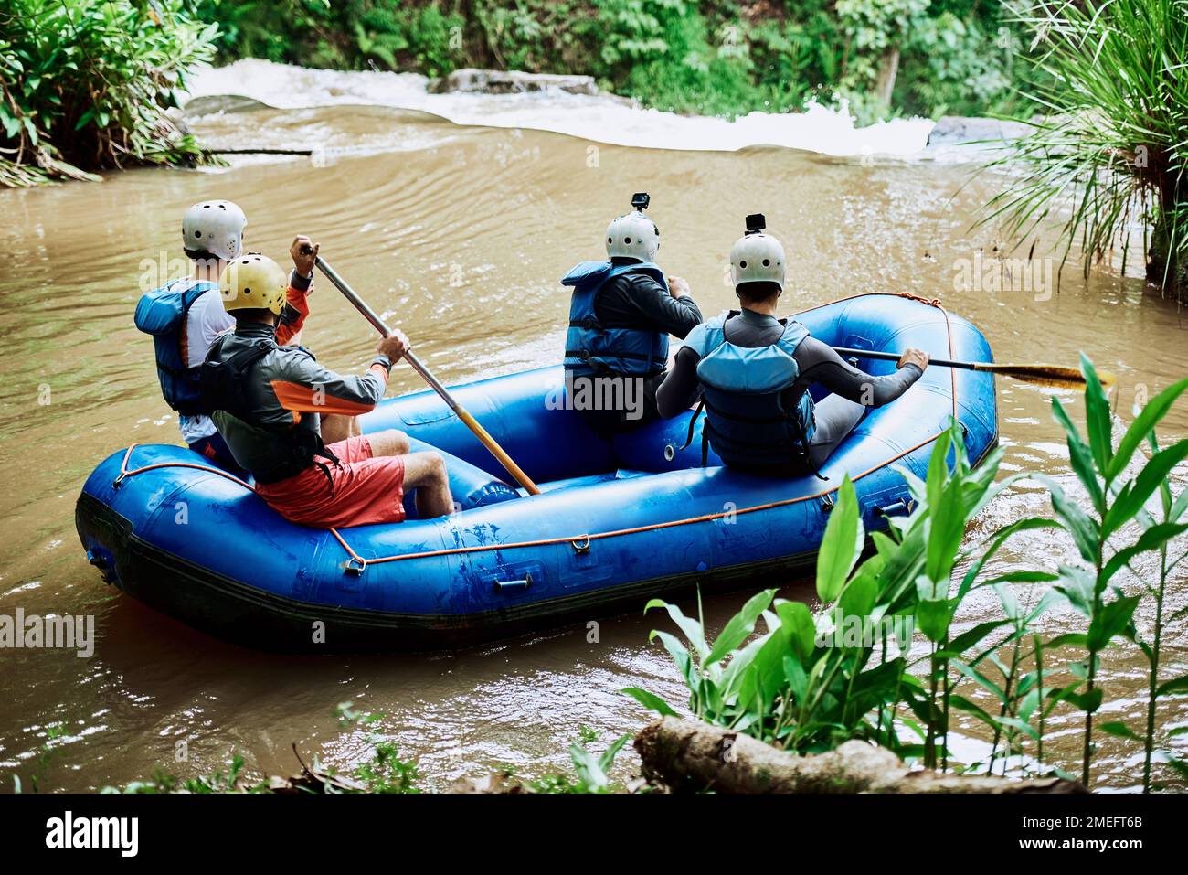 Was für ein sanftes Paddeln den Fluss hinunter. Rückblick auf eine Gruppe von unbekannten Menschen, die zusammen auf einem Gummischiff einen friedlichen Fluss entlang paddeln Stockfoto