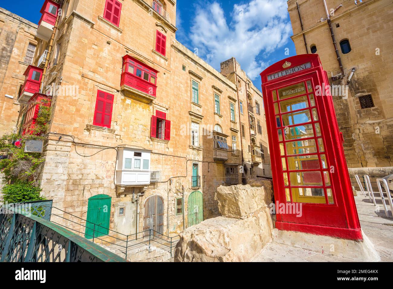 Valletta, Malta – Alte Straße von Valletta mit einer berühmten britischen roten Telefonzelle und traditionellen Balkonen und blauem Himmel an einem sonnigen Sommertag Stockfoto