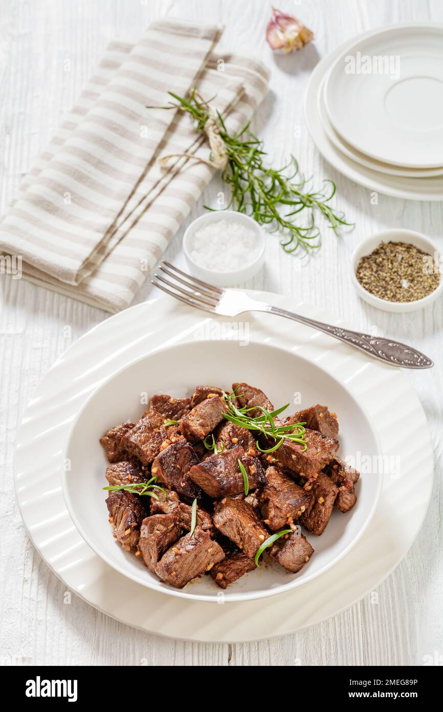 Gebratene saftige New york Strip Steak Bissen mit Butter, Rosmarin und Knoblauch in der Schüssel auf weißem Holztisch, vertikale Ansicht Stockfoto