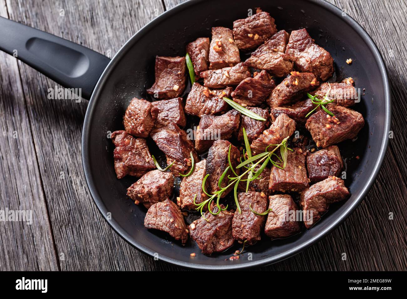 Gebratene saftige New yorker Steak-Bissen mit Butter, Rosmarin und Knoblauch auf Pfannkuchen auf einem dunklen Holztisch Stockfoto