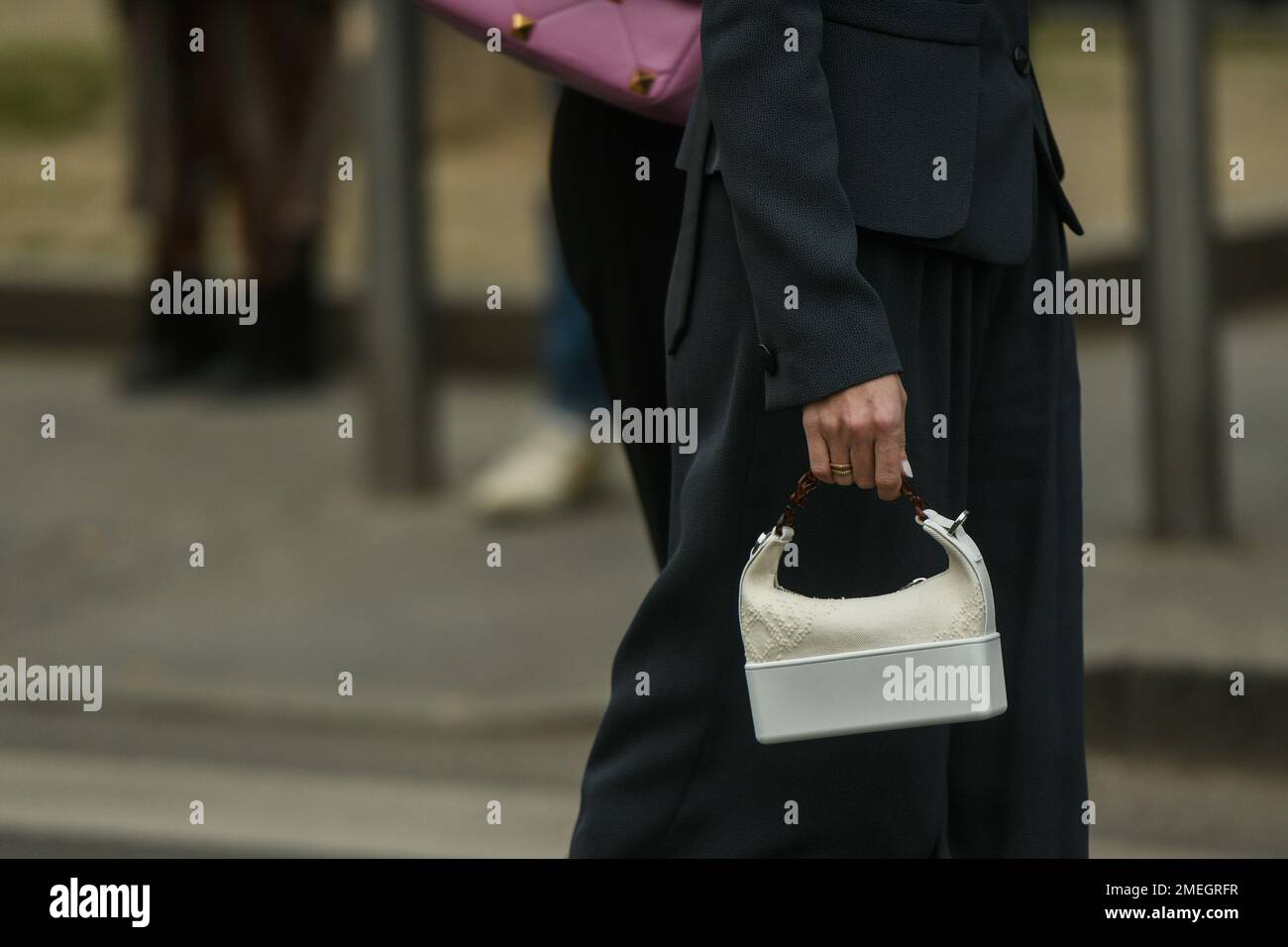 Mailand, Italien - 24. Februar 2022: Frau, die auf der Straße läuft, trägt eine schwarze Jacke und weite Hosen mit weißer Handtasche. Stockfoto