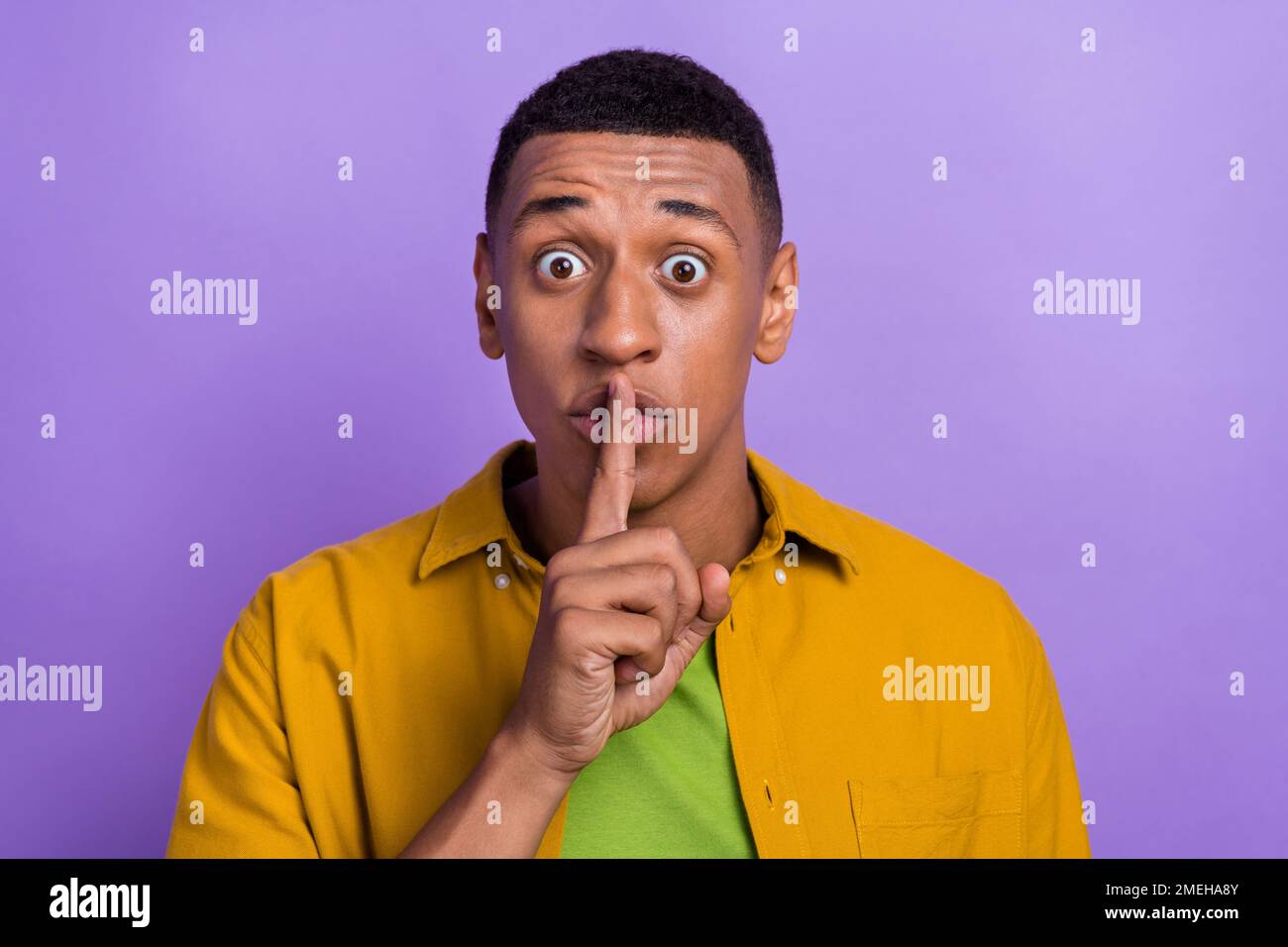 Porträt von lustigen positiven guten Laune Mann tragen gelbe Kleidung halten Finger auf Lippen halten Augen weit offen isoliert auf violettem Hintergrund Stockfoto