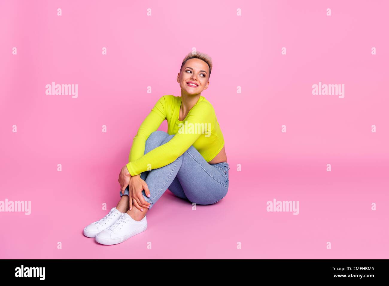 Großes Foto einer attraktiven jungen Frau, die sich im Sitzen die Knie umarmt und leer aussieht elegantes gelbes Outfit isoliert auf pinkfarbenem Hintergrund Stockfoto