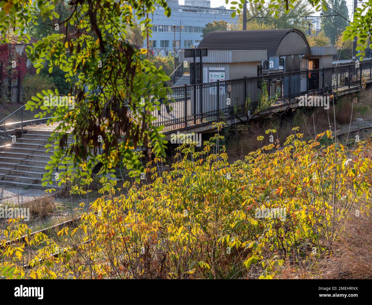 Vorstadtbahnhof mit Betonplattform und Metallschuppen. Farbenfroher Herbstmorgen. Stockfoto