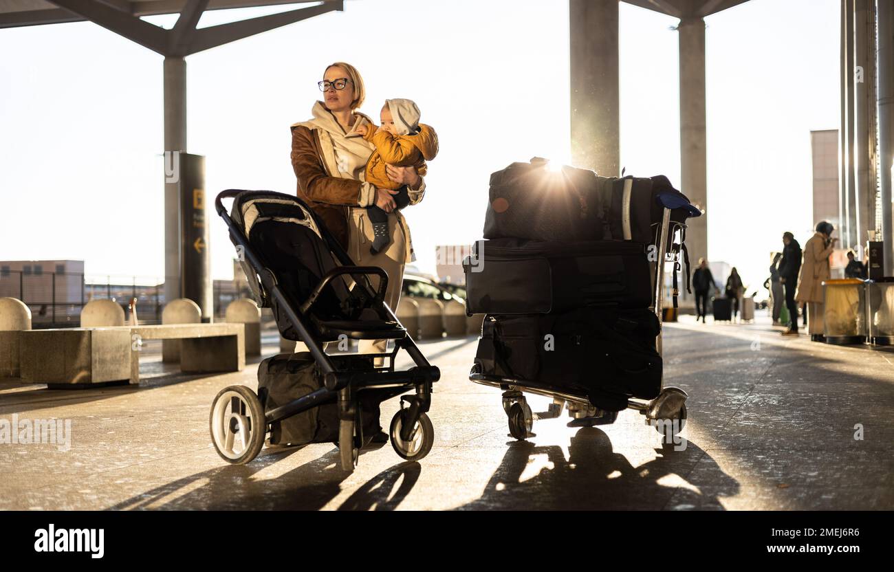 Mutter reist mit seinem kleinen Jungen, geht, schiebt Kinderwagen und Gepäckwagen vor die Flughafenstation Stockfoto