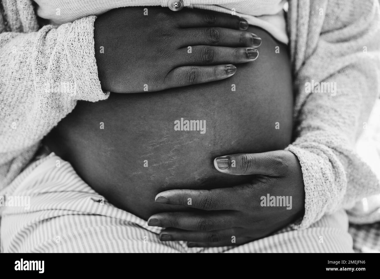 Nahaufnahme einer afrikanischen schwangeren Frau, die ihren Bauch hält - Fokus auf die Hände - Schwarz-Weiß-Schnitt Stockfoto