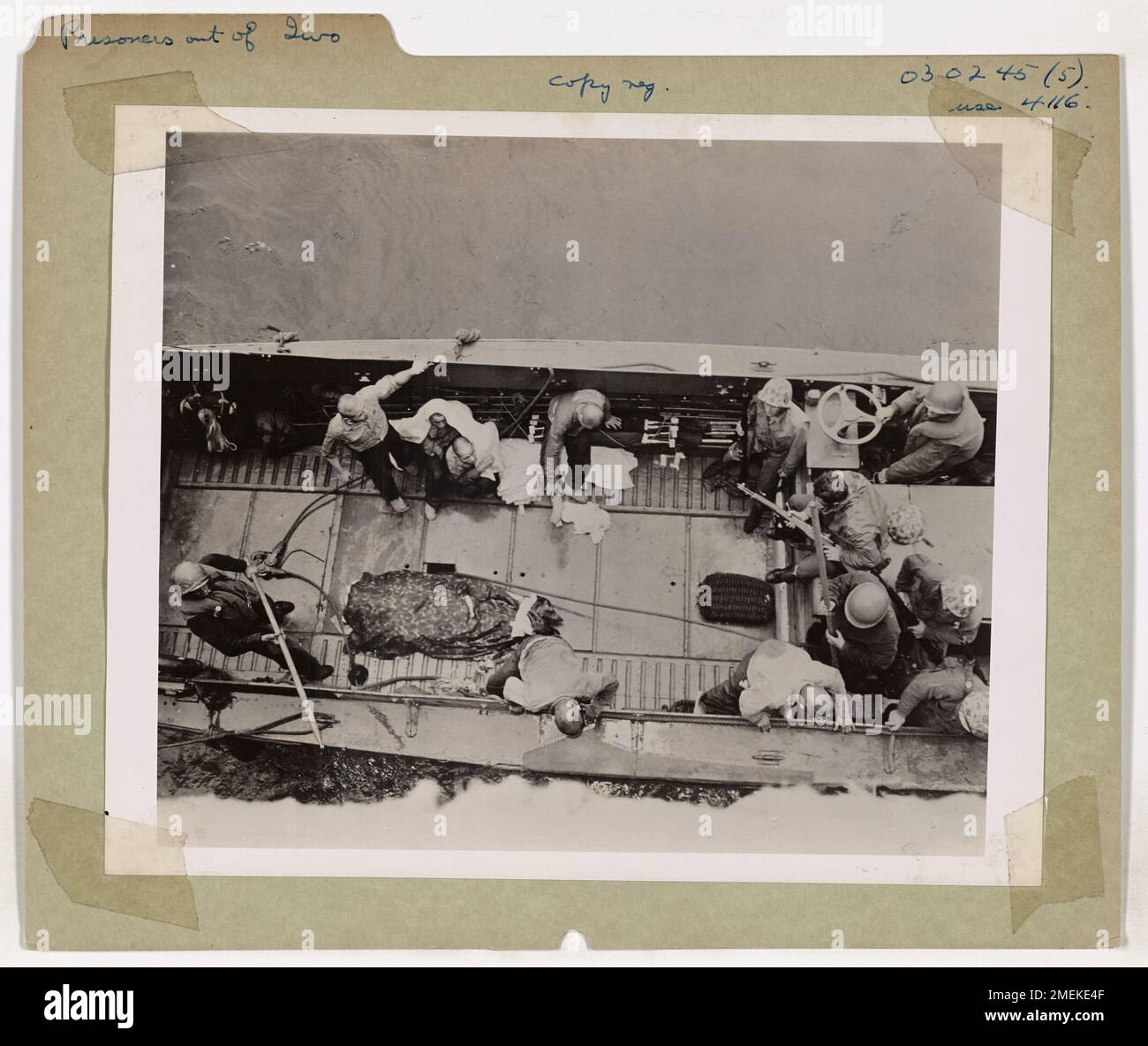 Sechs japanische Gefangene, die während der Schlacht von Iwo Jima gefangen genommen wurden, werden in einem Landeboot herausgeholt und sind bereit, die Landennetze eines von der Küstenwache bemannten Invasionsschiffs zu erklimmen. Die Leiche eines Marine liegt auf dem Deck, eine düstere Erinnerung an den heftigen Kampf, der zur Gefangennahme dieser Gefangenen führte. Stockfoto