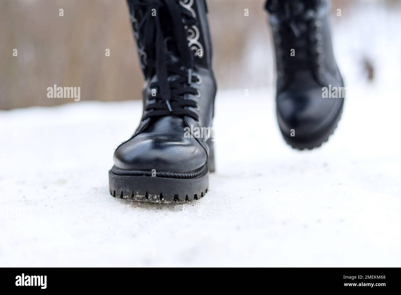 Weibliche Beine in schwarzen Lederstiefeln zum Schnüren auf schneebedeckten Wegen. Frau läuft auf der Winterstraße, rutschig bei kaltem Wetter Stockfoto