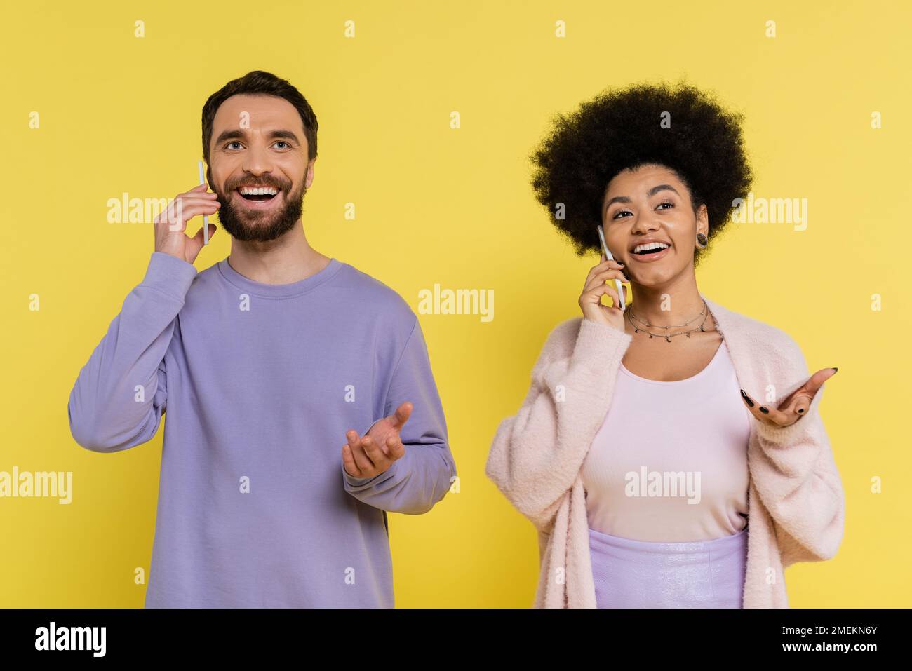 Trendiges und positives interrassenbezogenes Paar, das mit einem Mobiltelefon spricht, isoliert auf Gelb Stockfoto