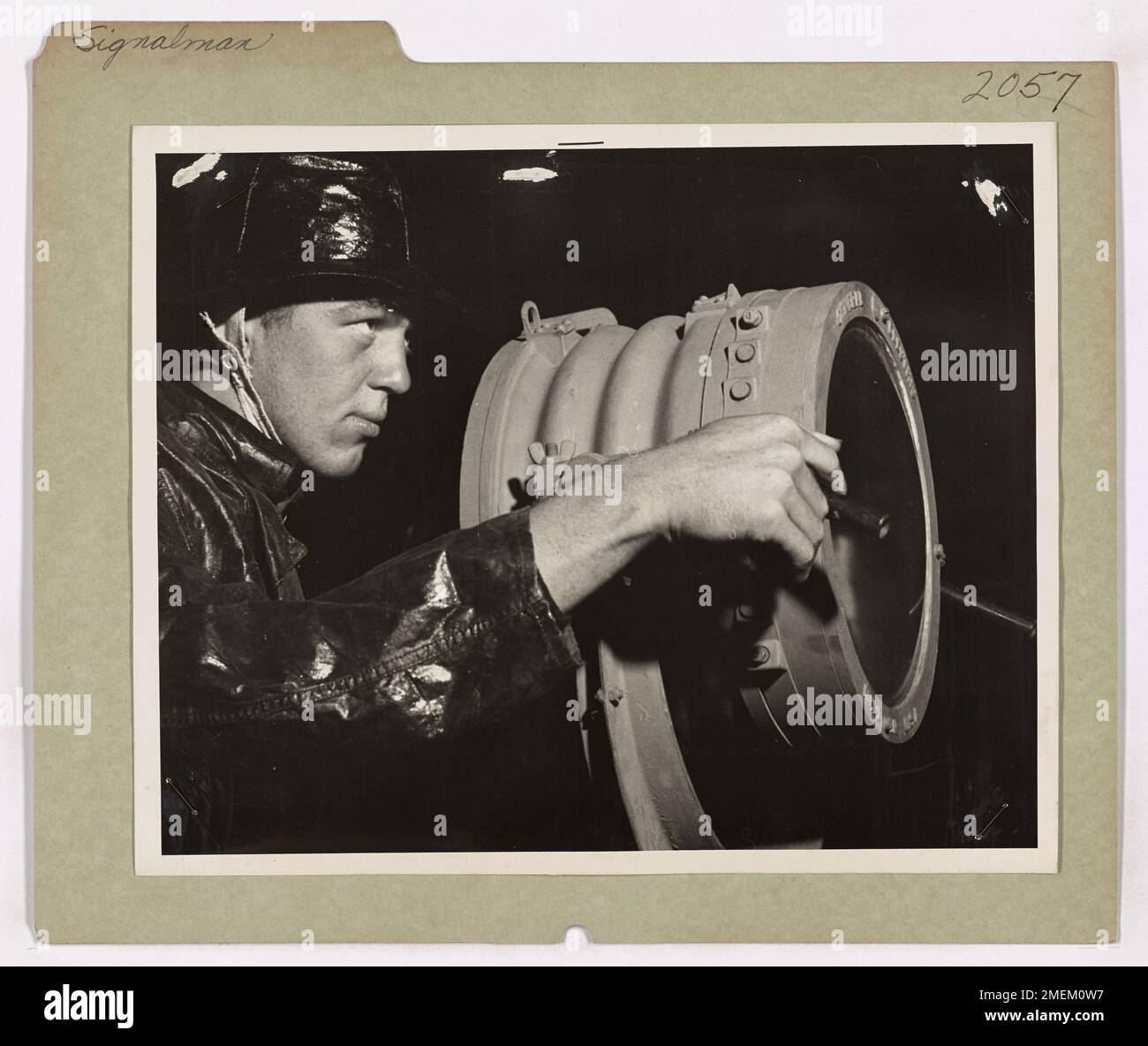 Ein Küstenwache-Signalmann an Bord eines Cutters sendet eine Sturmwarnung an Handelsschiffe, da ein nordatlantischer Sturm einen alliierten Konvoi bedroht. Das Schneidwerk spielt eine wichtige Rolle bei der Gewährleistung eines sicheren Durchgangs unter gefährlichen Bedingungen. Stockfoto