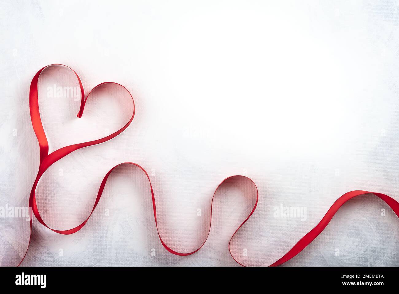 Rotes Band in Herzform auf klassischem weiß-grauen Hintergrund. Festliches Konzept für den Valentinstag. Draufsicht mit Kopierbereich. Stockfoto